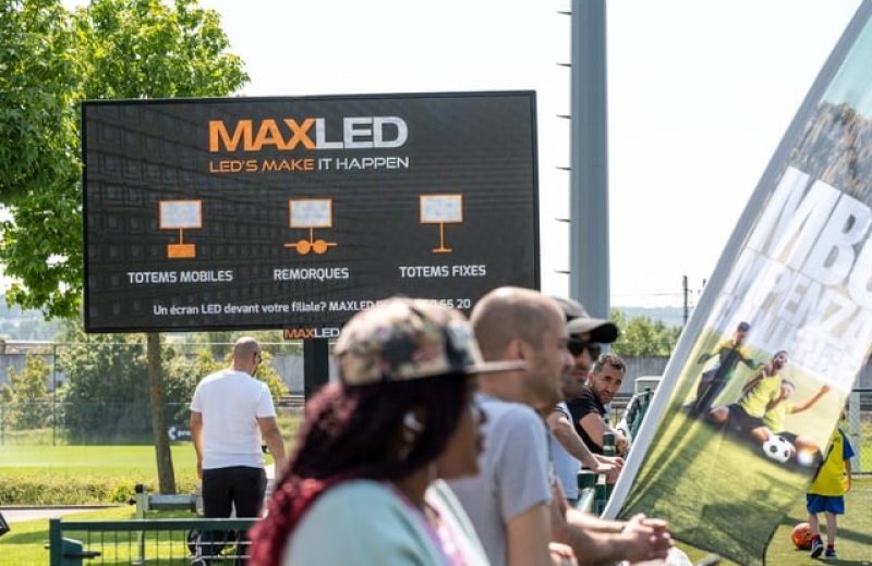 Groot mobiel ledscherm van MaxLED langs een voetbalveld, met toeschouwers ervoor